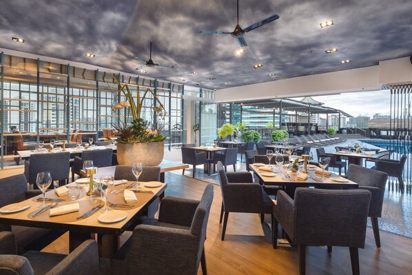 A modern restaurant with high ceilings, large windows, and a view of the cityscape.