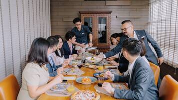 A group of people dining at a wooden table in a room with brick walls and a large mirror.