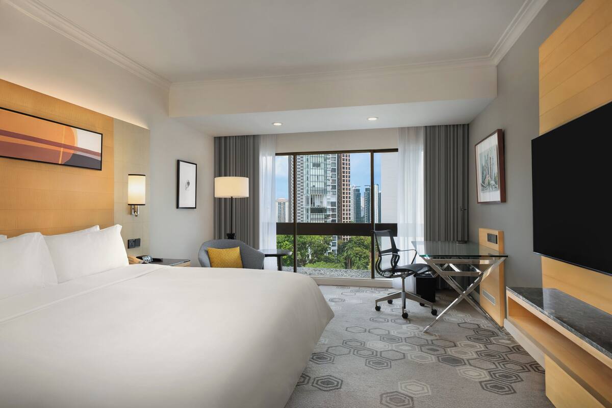 Habitación de hotel con una cama grande, un escritorio con silla, un televisor y vistas a la ciudad.