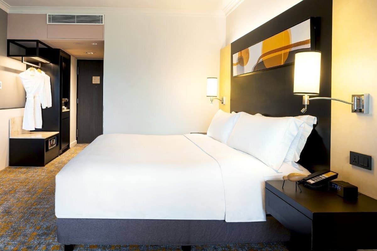 Una habitación de hotel con una cama grande, una mesita de noche con teléfono, un televisor montado en la pared, un armario y un espejo.