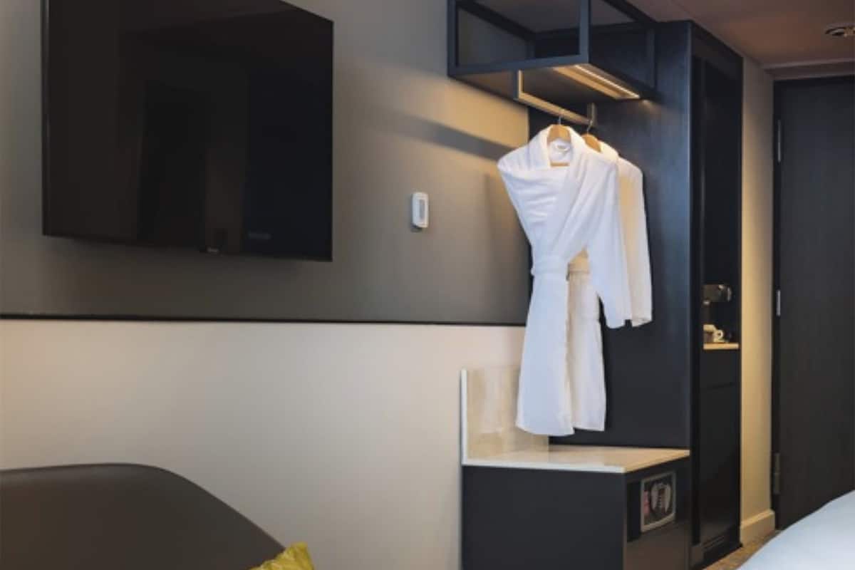 Una habitación de hotel con cama, mesita de noche, perchero, espejo y armario.