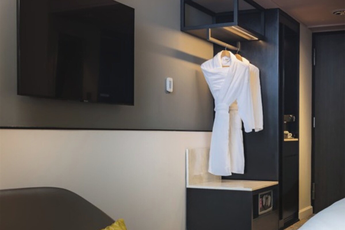 Une chambre d’hôtel comprenant un lit, une table de chevet, une robe suspendue, un miroir et une armoire.