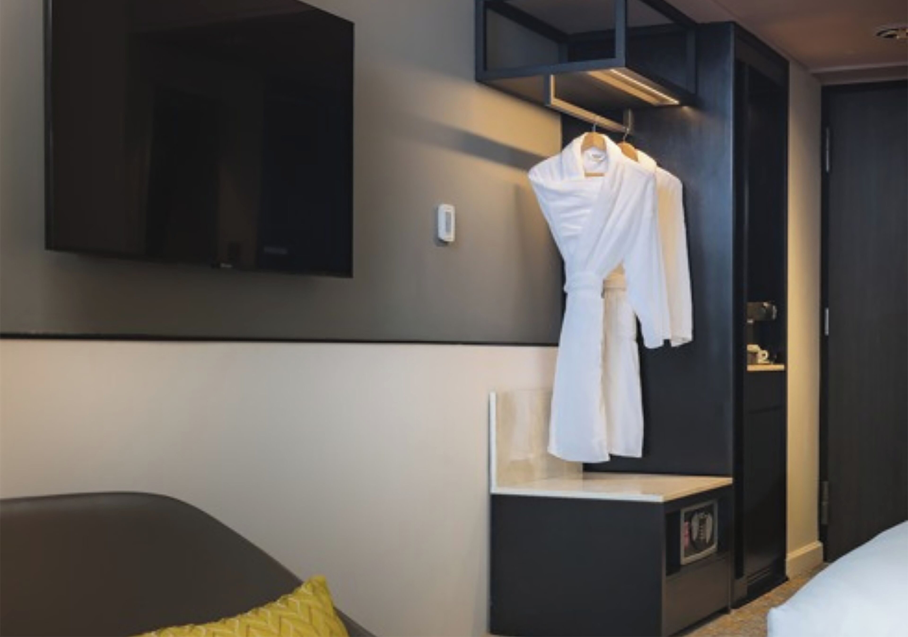 A hotel room with a bed, a bedside table, a hanging robe, and a mounted television.