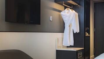 A hotel room with a bed, a bedside table, a hanging robe, and a mounted television.