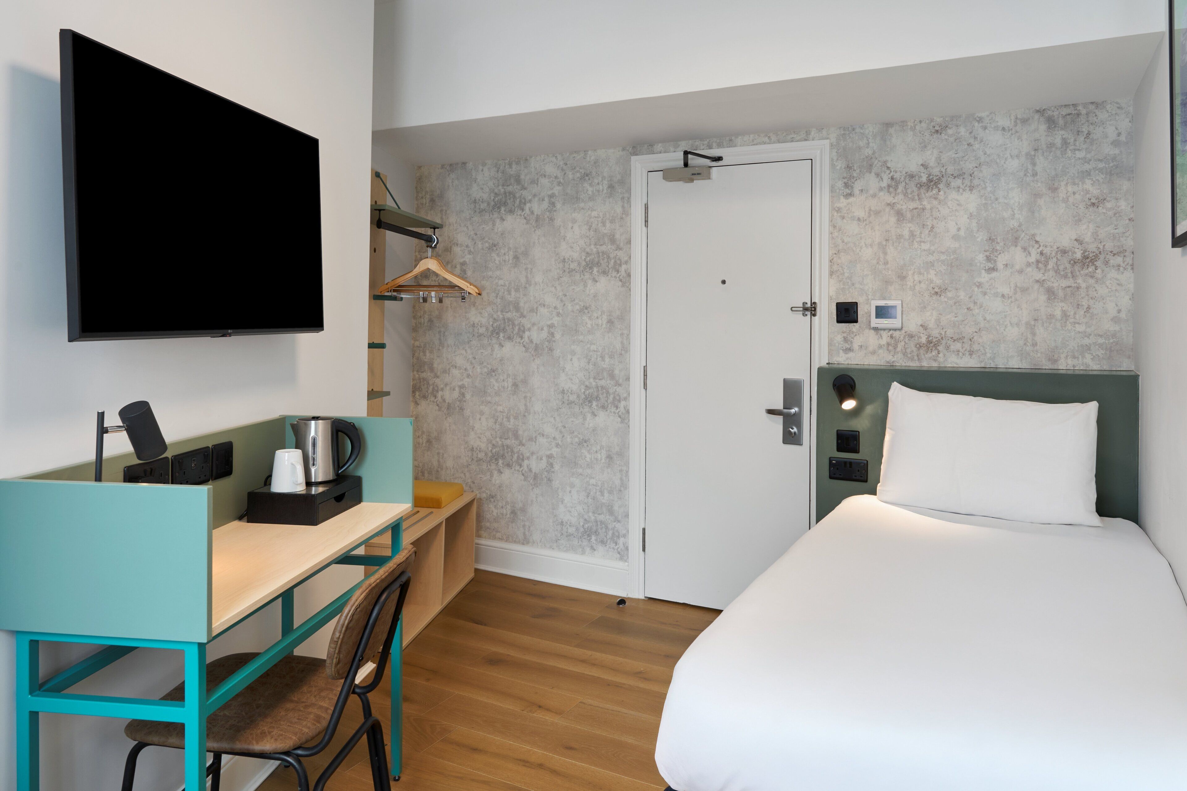 Une chambre d’hôtel avec un lit, un bureau et une chaise, une télévision et une porte.