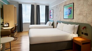 Une chambre d’hôtel avec deux lits, un bureau, une chaise, une petite table et une table de chevet.
