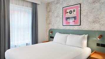 Una habitación de hotel con una cama grande, un cabecero con luces empotradas en la pared, un cuadro enmarcado y una ventana con cortinas.