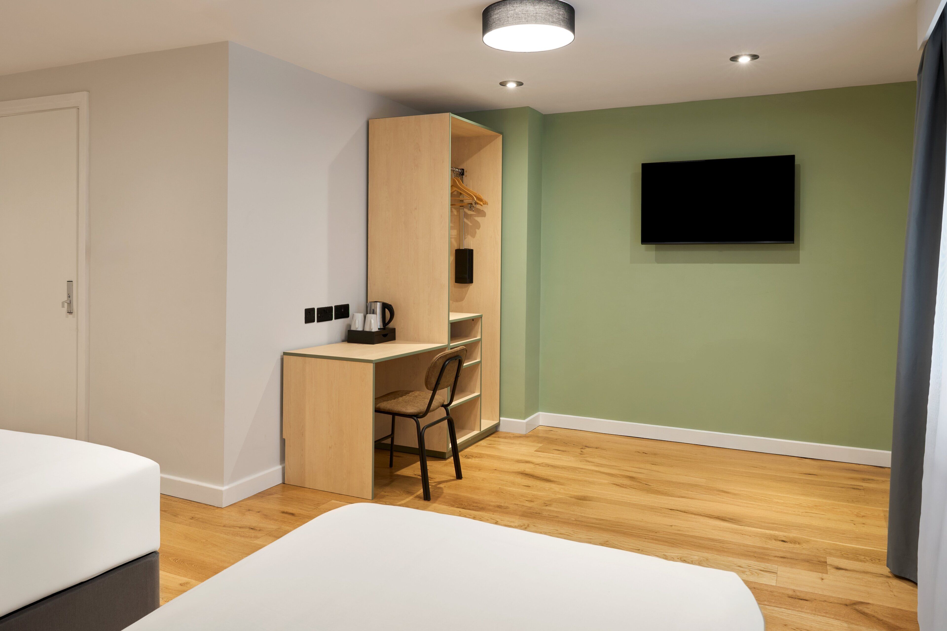 Una habitación de hotel moderna con un escritorio de madera, una silla, una cama y un televisor montado en la pared.