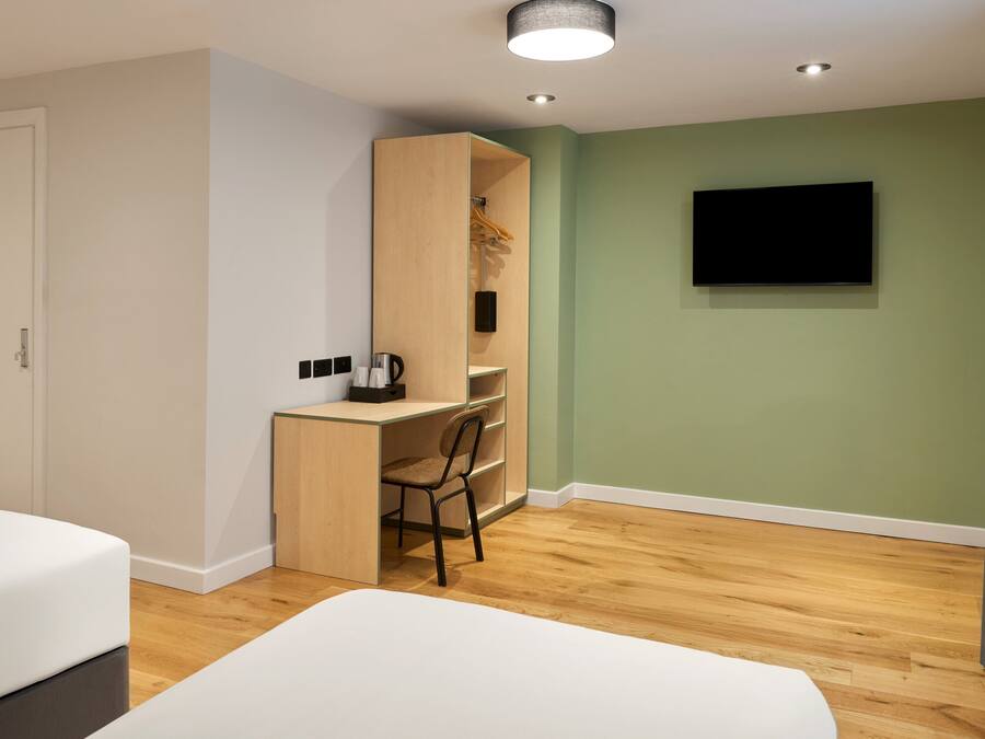 Una habitación de hotel moderna con un escritorio de madera, una silla, una cama y un televisor montado en la pared.