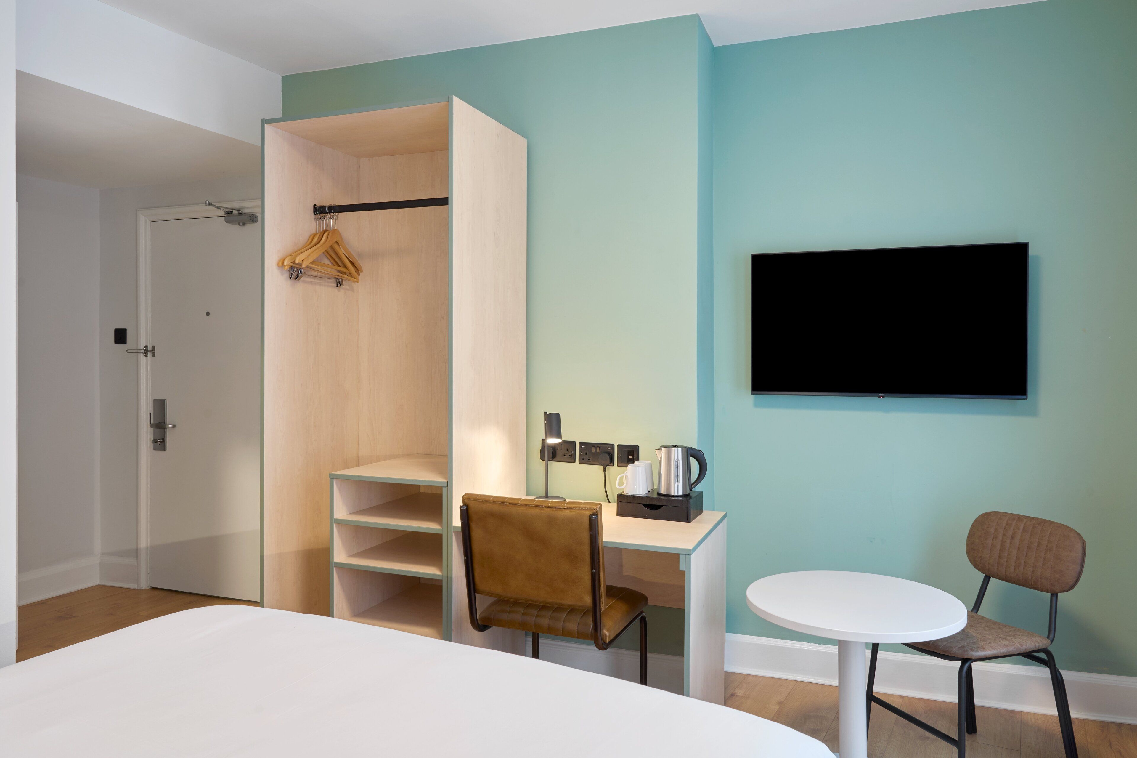 Een moderne hotelkamer met een bed, een bureau met stoel, een televisie en een kledingkast.