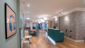 Un hall d’hôtel moderne avec un plancher en bois, un comptoir d’accueil de couleur turquoise et des œuvres d’art encadrées accrochées aux murs.