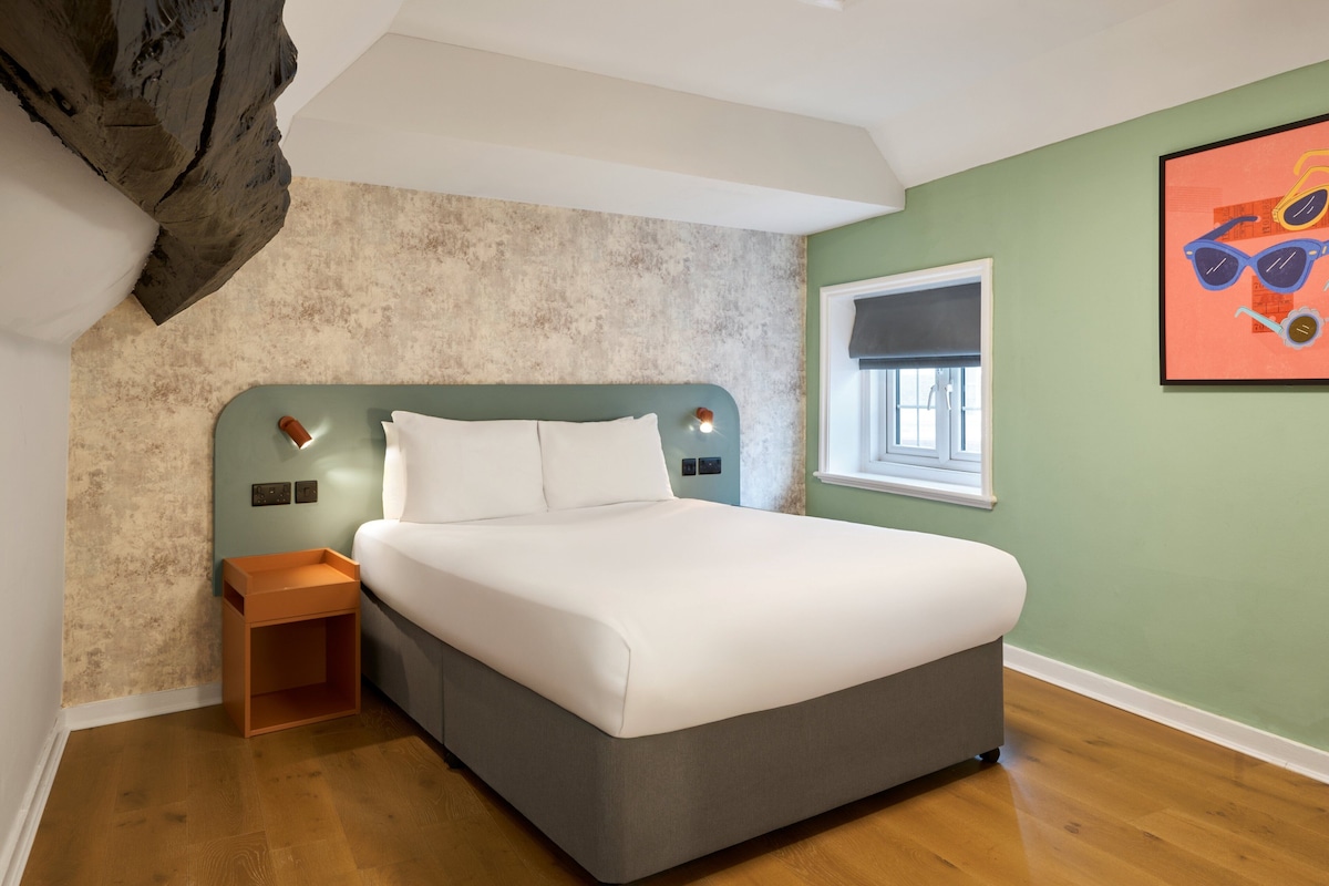 A bedroom with a bed, nightstand, and a wall-mounted light fixture.