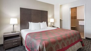 A hotel room with a large bed, two bedside tables with lamps, a wooden headboard, a walk-in closet, and a bathroom with a shower and toilet. - Ramada by Wyndham Monterey (Monterey)