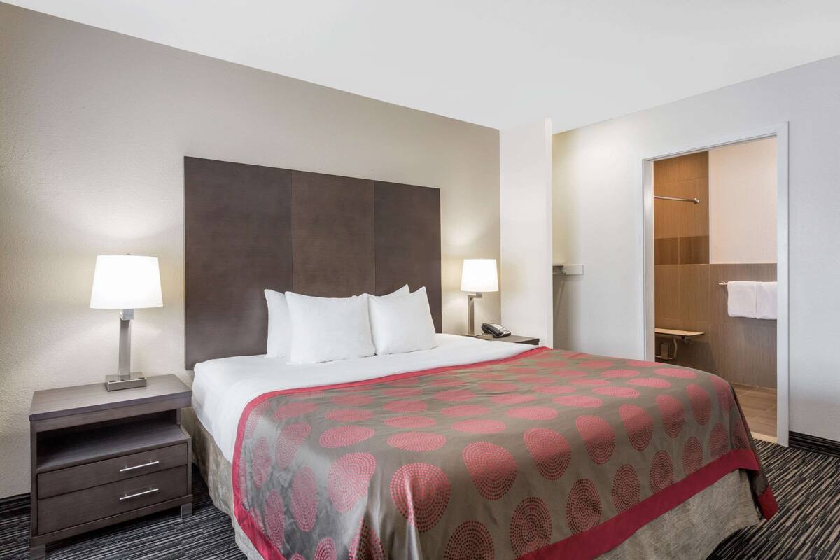 A hotel room with a large bed, two bedside tables with lamps, a wooden headboard, a walk-in closet, and a bathroom with a shower and toilet.