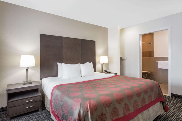 A hotel room with a large bed, two bedside tables with lamps, a wooden headboard, a walk-in closet, and a bathroom with a shower and toilet.