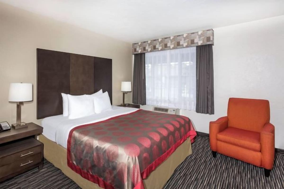 A hotel room with a large bed, a nightstand, a chair, and a window with curtains.