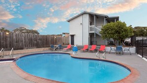 A swimming pool with a brick edge, surrounded by red and blue lounge chairs. - Ramada by Wyndham Monterey (Monterey)