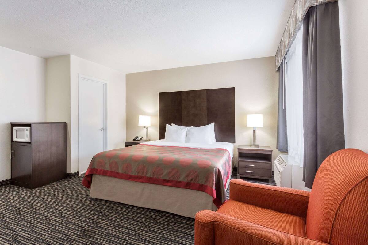 A hotel room with a bed, two bedside tables, a chair, a desk, a microwave, and a wardrobe.