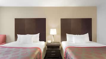 A hotel room with two beds, a nightstand with a lamp, and a small drawer.