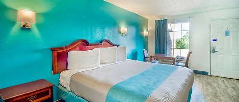 A hotel room with a bed, a nightstand, a desk, and a window with curtains.