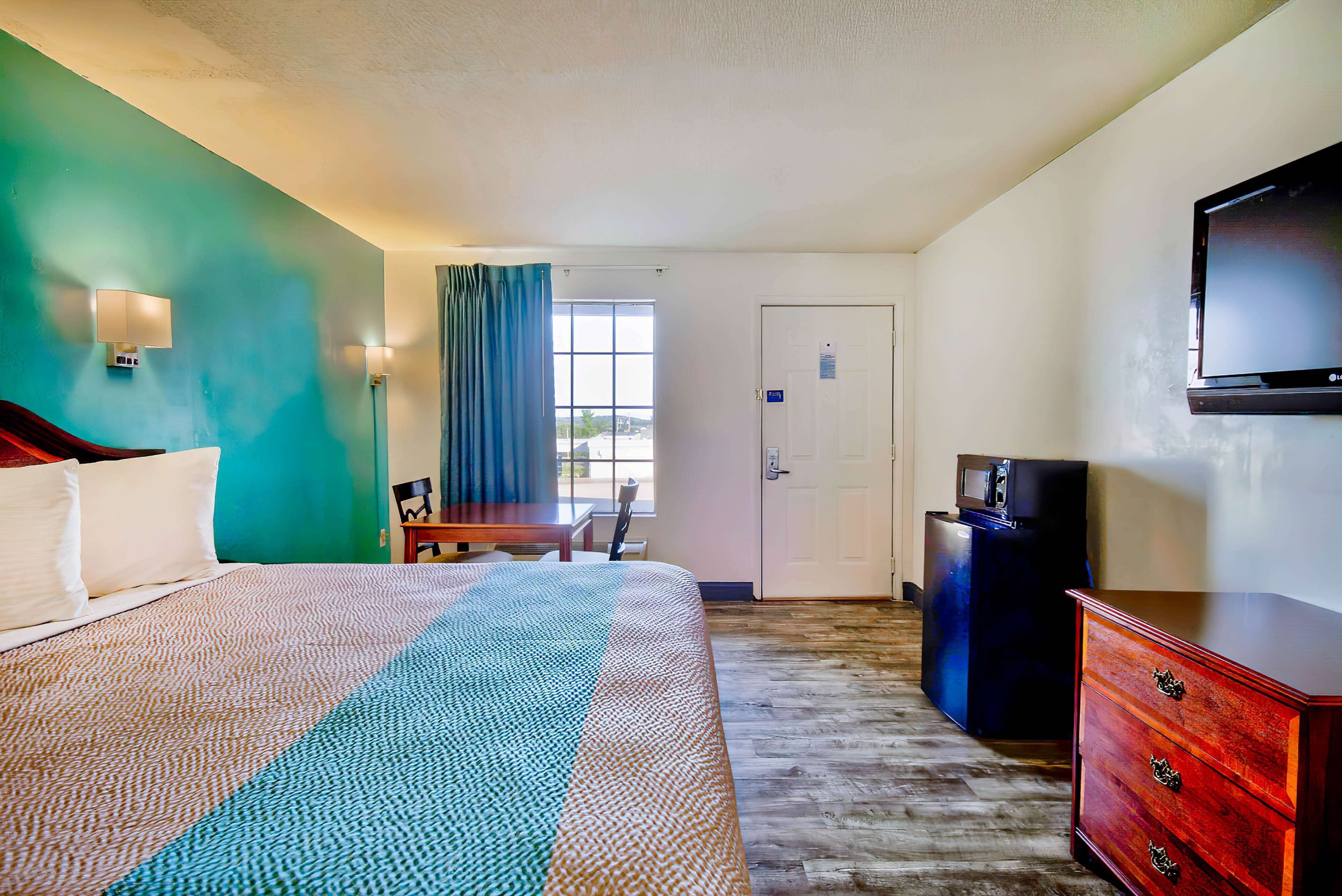 A hotel room with a bed, a desk, a dresser, a television, and a door.