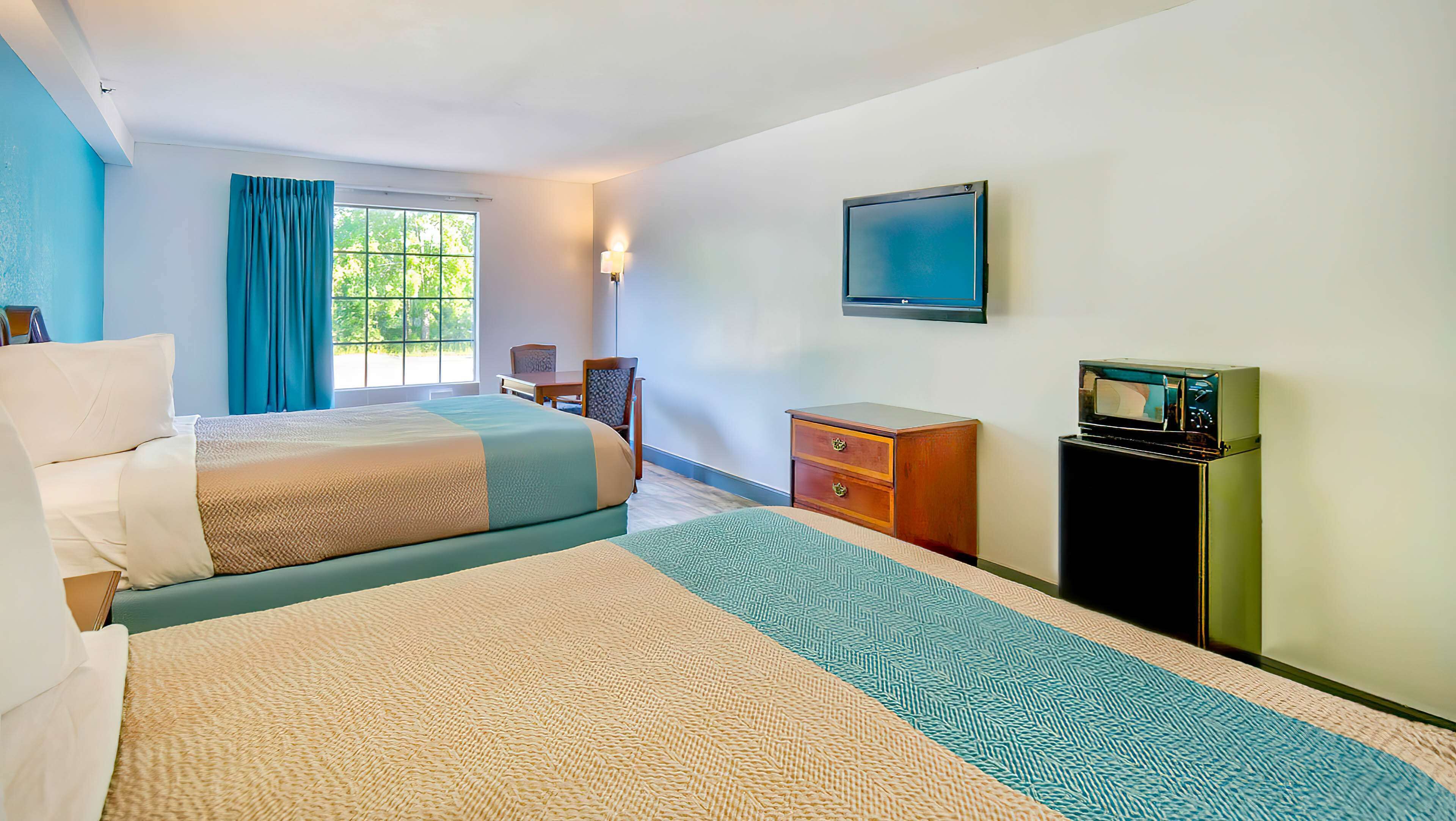 A hotel room with two beds, a desk, a chair, a dresser, a television, and a window with curtains.