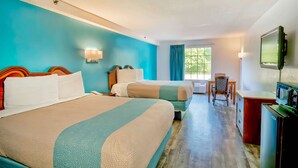 A hotel room with two beds, a desk, a chair, a television, and a window with curtains.