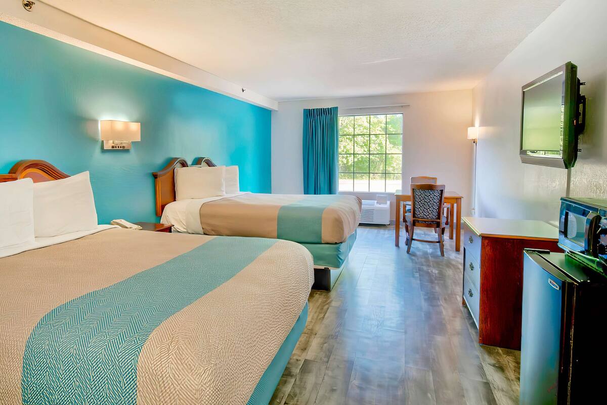 Une chambre d’hôtel avec deux lits, un bureau, une chaise, une télévision et une fenêtre avec des rideaux.