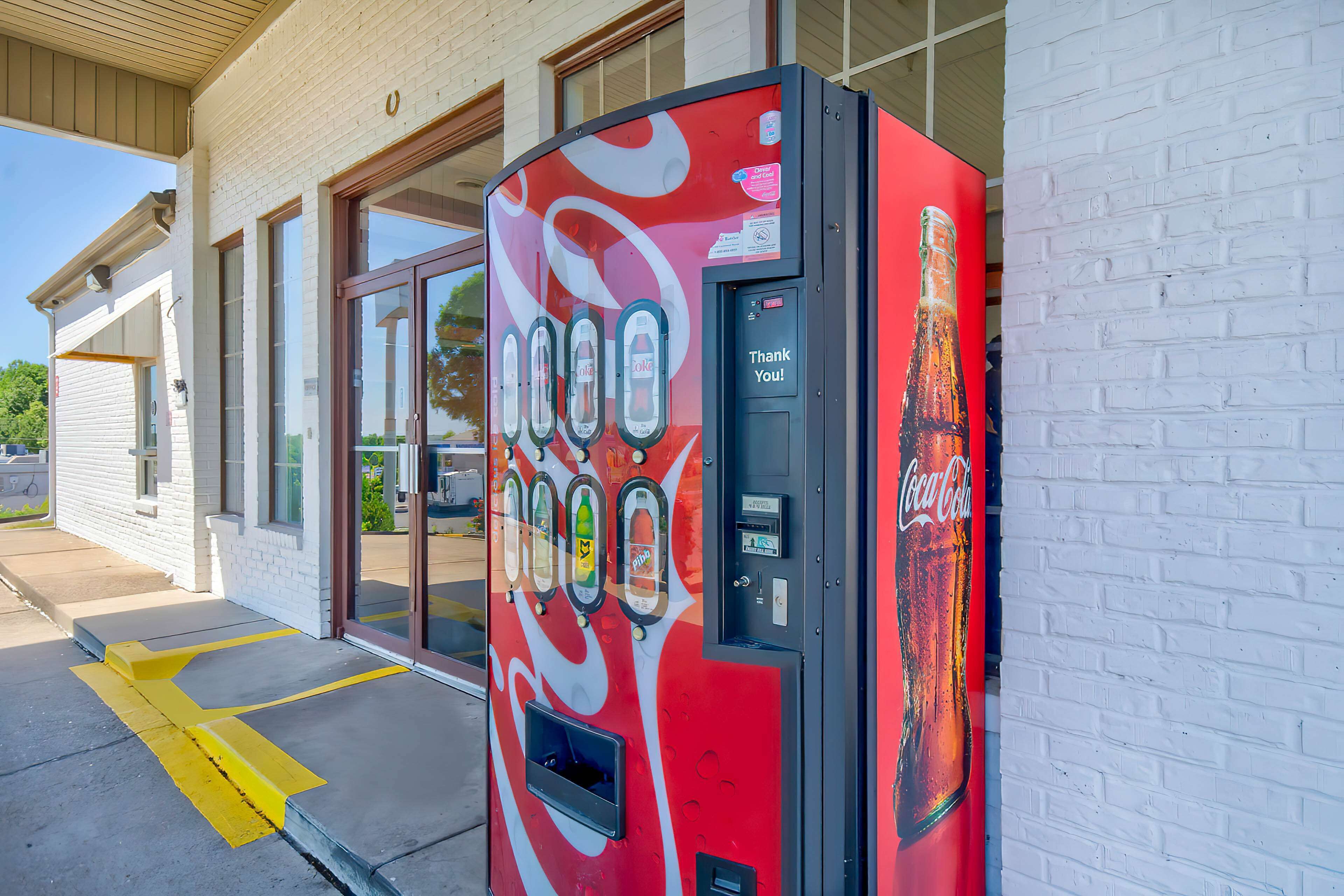 A Coca-Cola branded vending machine outside a building with large windows and a brick facade.