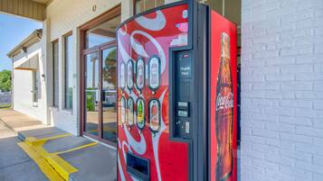Een Coca-Cola automaat buiten een gebouw met grote ramen en een bakstenen gevel.