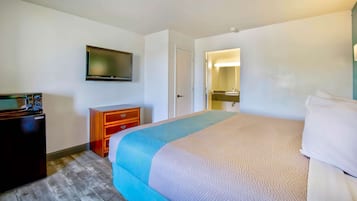 A hotel room with a bed, a dresser, a television, and a bathroom visible through an open door.