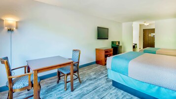 Habitación de hotel con cama, escritorio, dos sillas, cómoda, televisor y puerta.