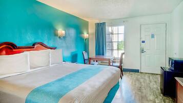 A hotel room with a bed, a desk, a chair, a television, and a door.