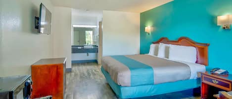 A hotel room with a bed, a desk, a mirror, and a TV.