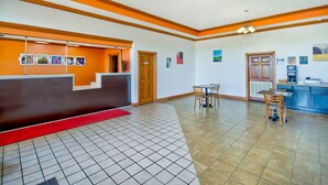 A hotel lobby with a reception desk, a small dining area with two tables and chairs, and a kitchen area with a coffee machine.