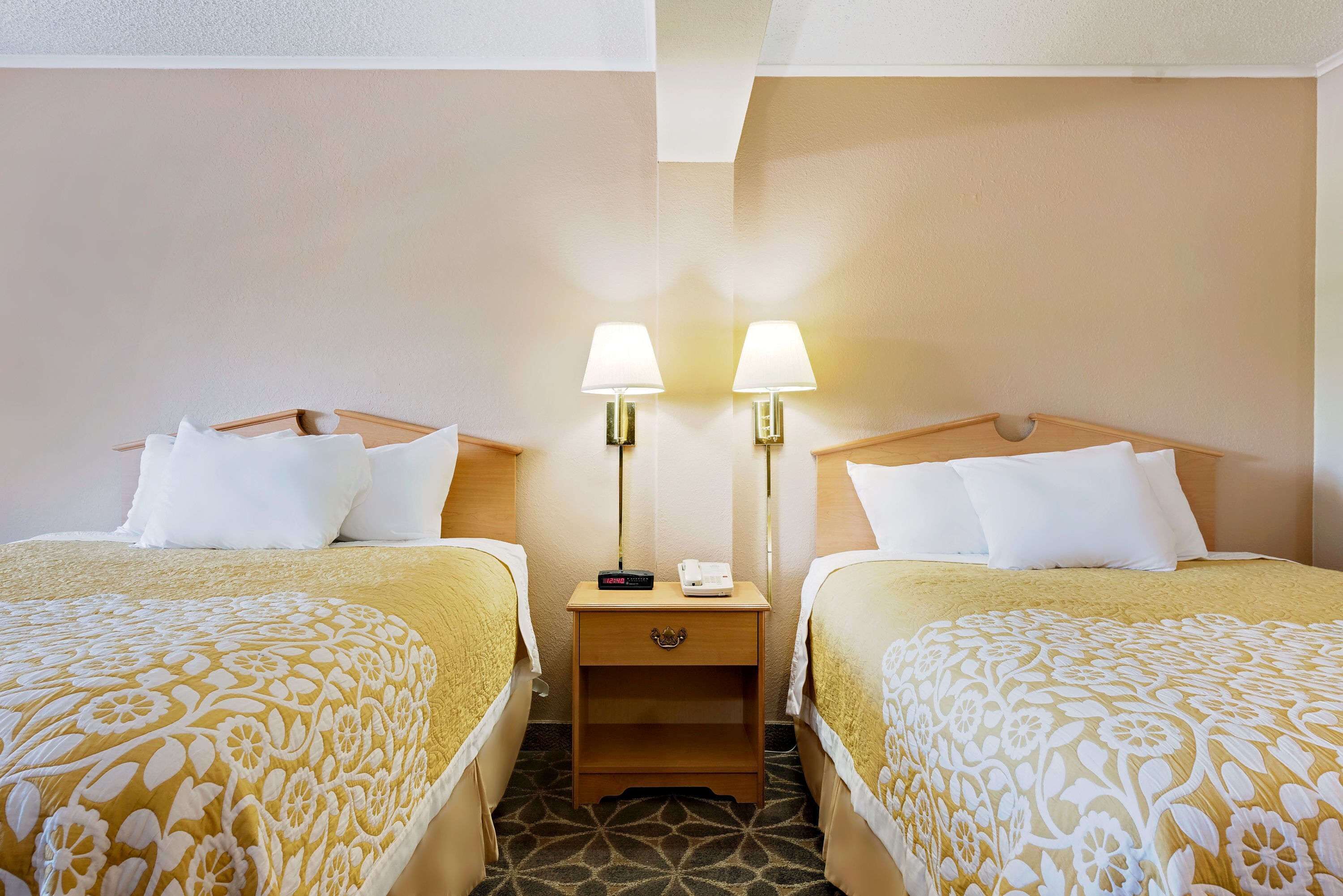 A hotel room with two beds, each with a patterned bedspread, a nightstand between them, and two bedside lamps.