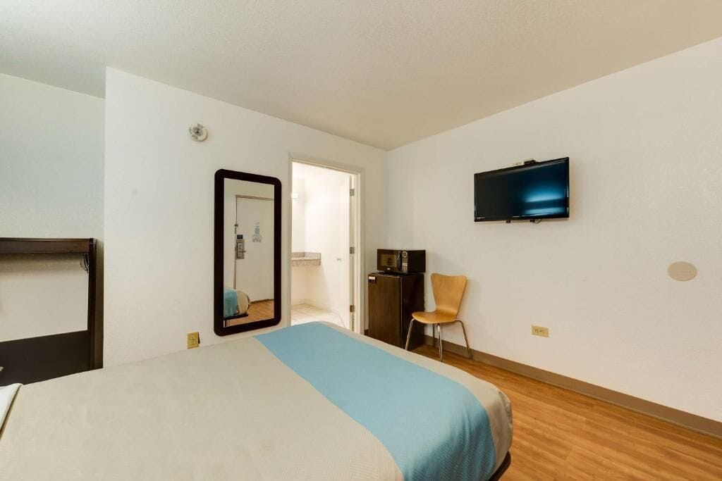 Una habitación de hotel con una cama, un televisor en la pared, una silla y un escritorio con un ordenador.