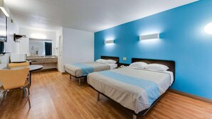 Habitación de hotel con dos camas individuales, un pequeño rincón americano, un comedor con mesa y sillas, y un baño visible a través de una puerta abierta.