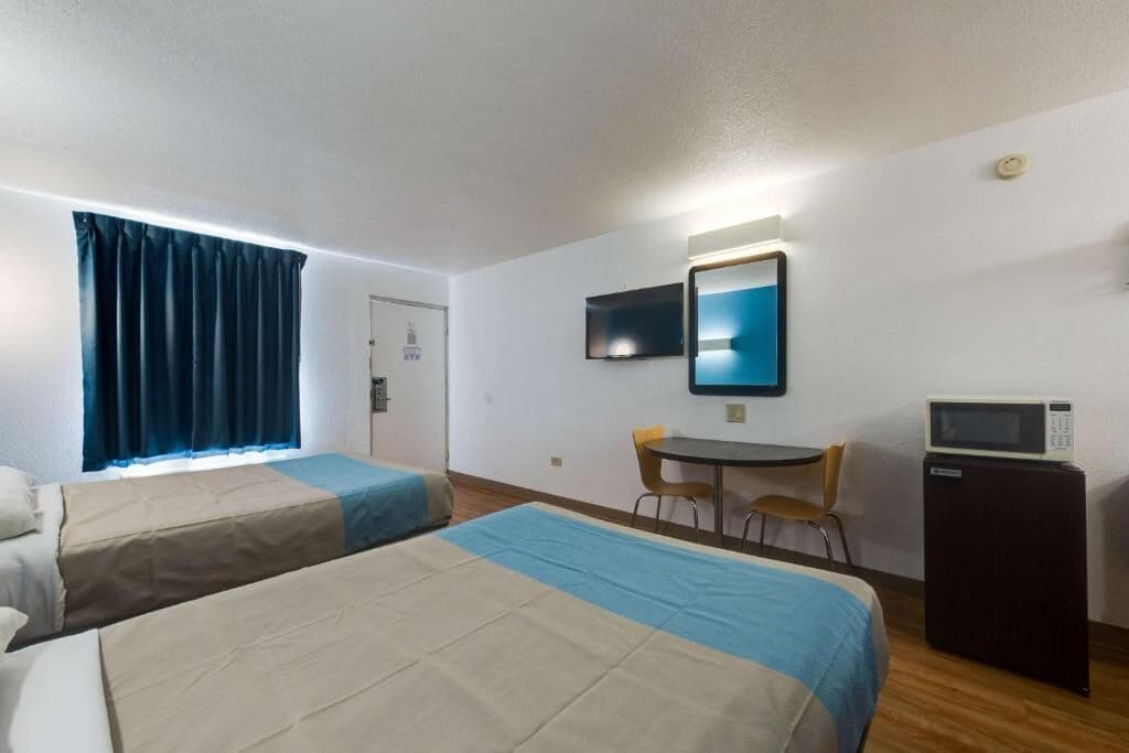 A hotel room with two beds, a desk, a chair, a TV, and a microwave.