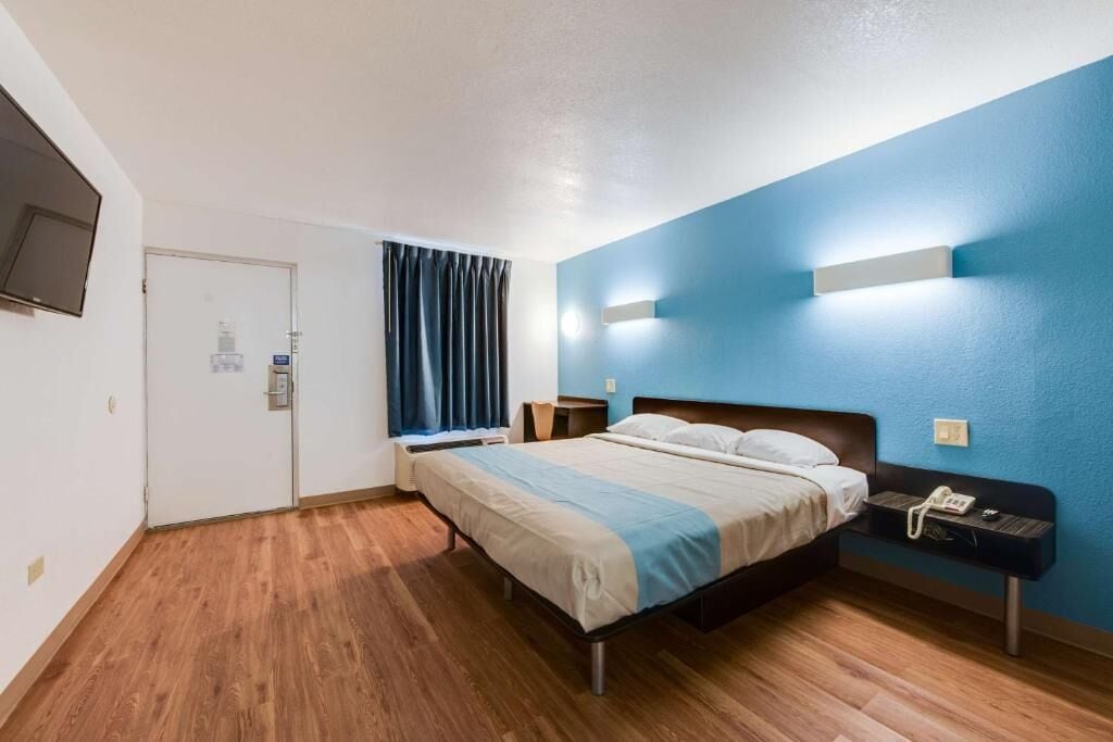 A hotel room with a bed, bedside table, and a TV mounted on the wall.
