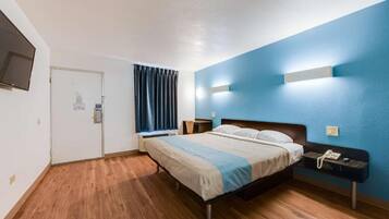 A hotel room with a bed, bedside table, and a TV mounted on the wall.