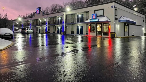 Un motel con un cartel con el número '6', un cartel de 'Bienvenido' y una zona cubierta con techo azul.