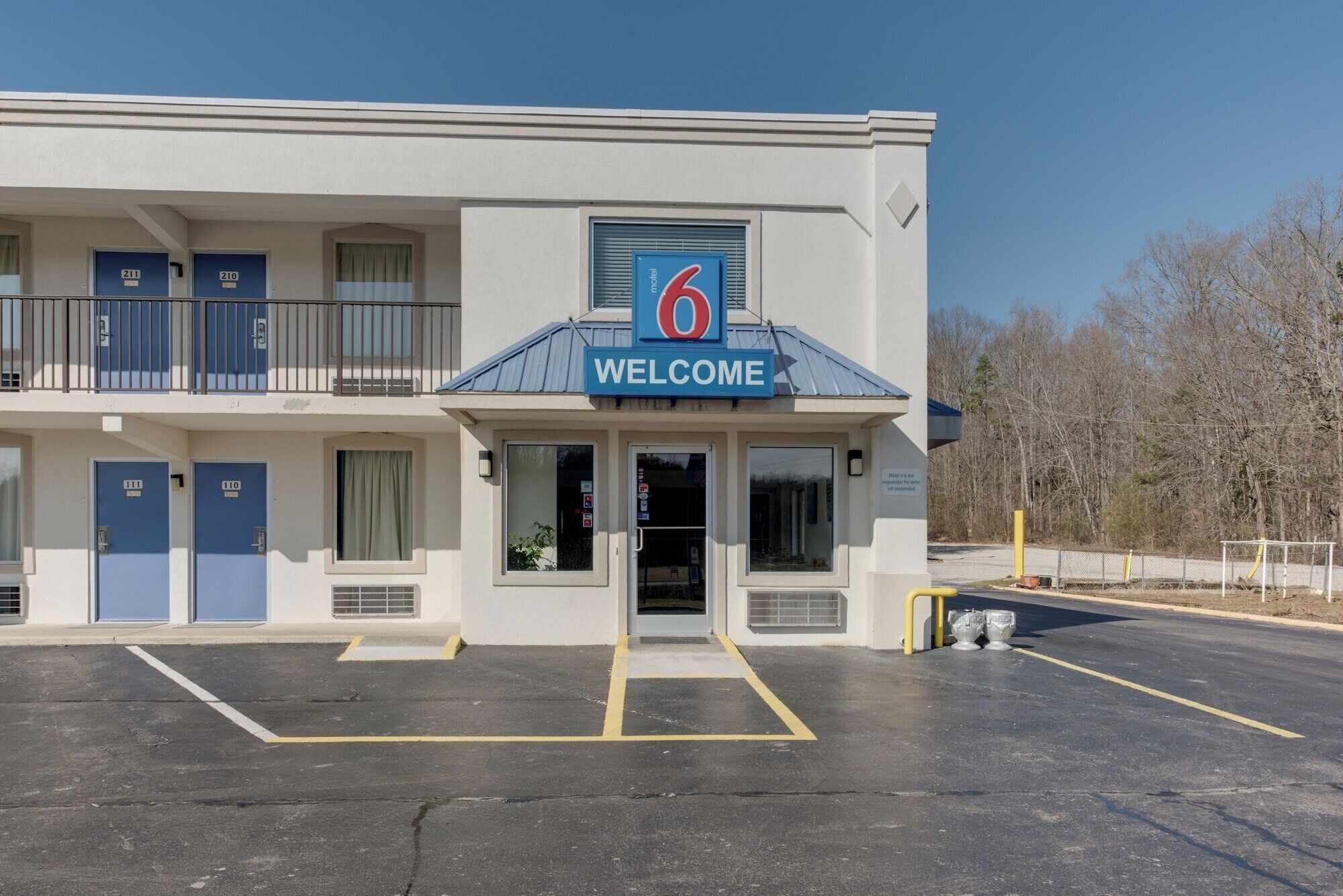 Un motel con un letrero que dice '6' y un cartel de 'BIENVENIDOS' sobre la entrada. Hay varias puertas azules, cada una con un número.