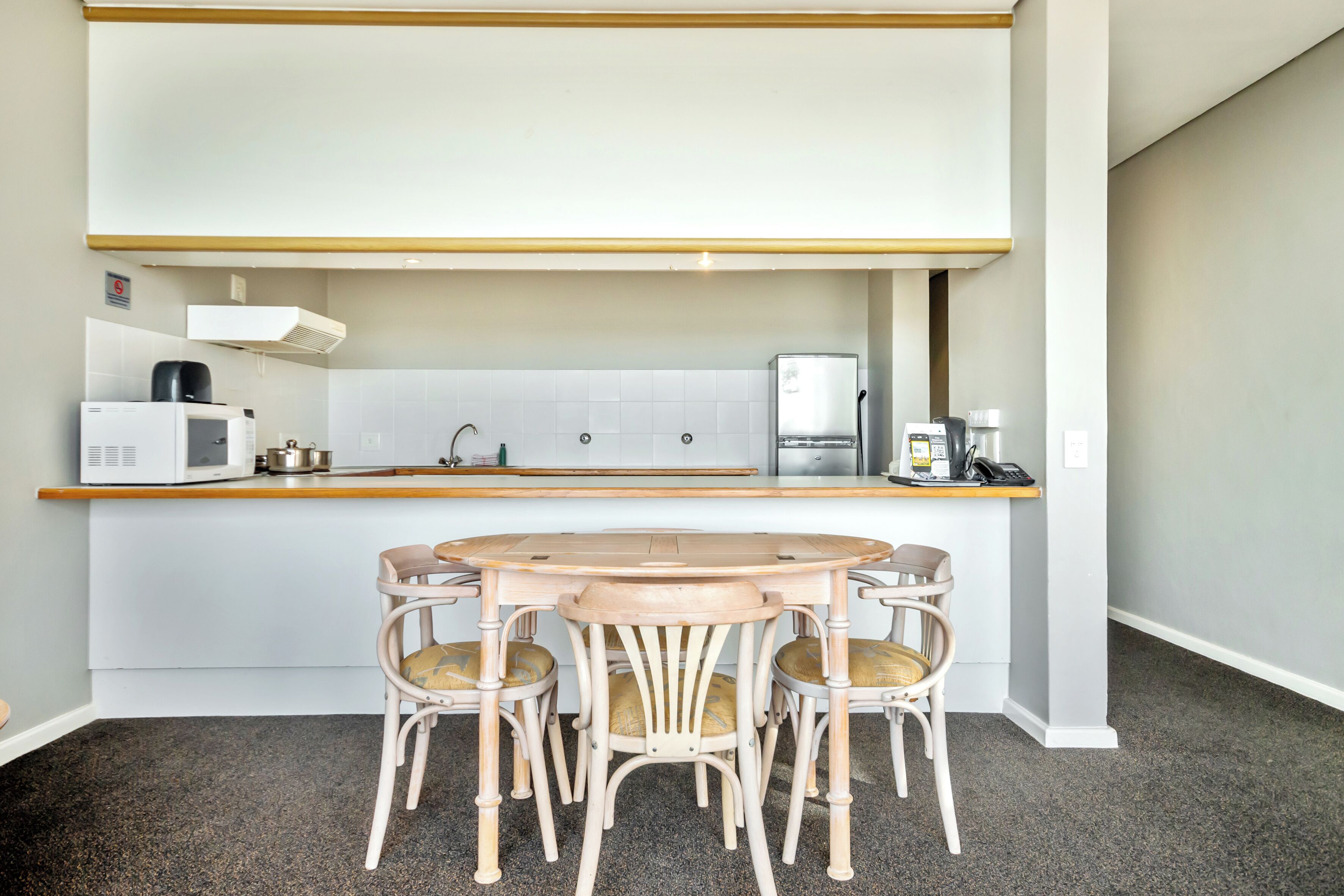 A compact kitchen with a round table and four chairs, a microwave, a coffee maker, and a refrigerator.
