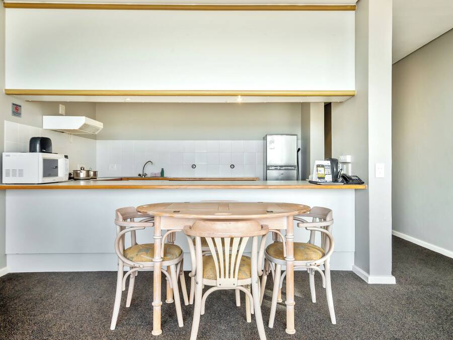 A compact kitchen with a round table and four chairs, a microwave, a coffee maker, and a refrigerator.