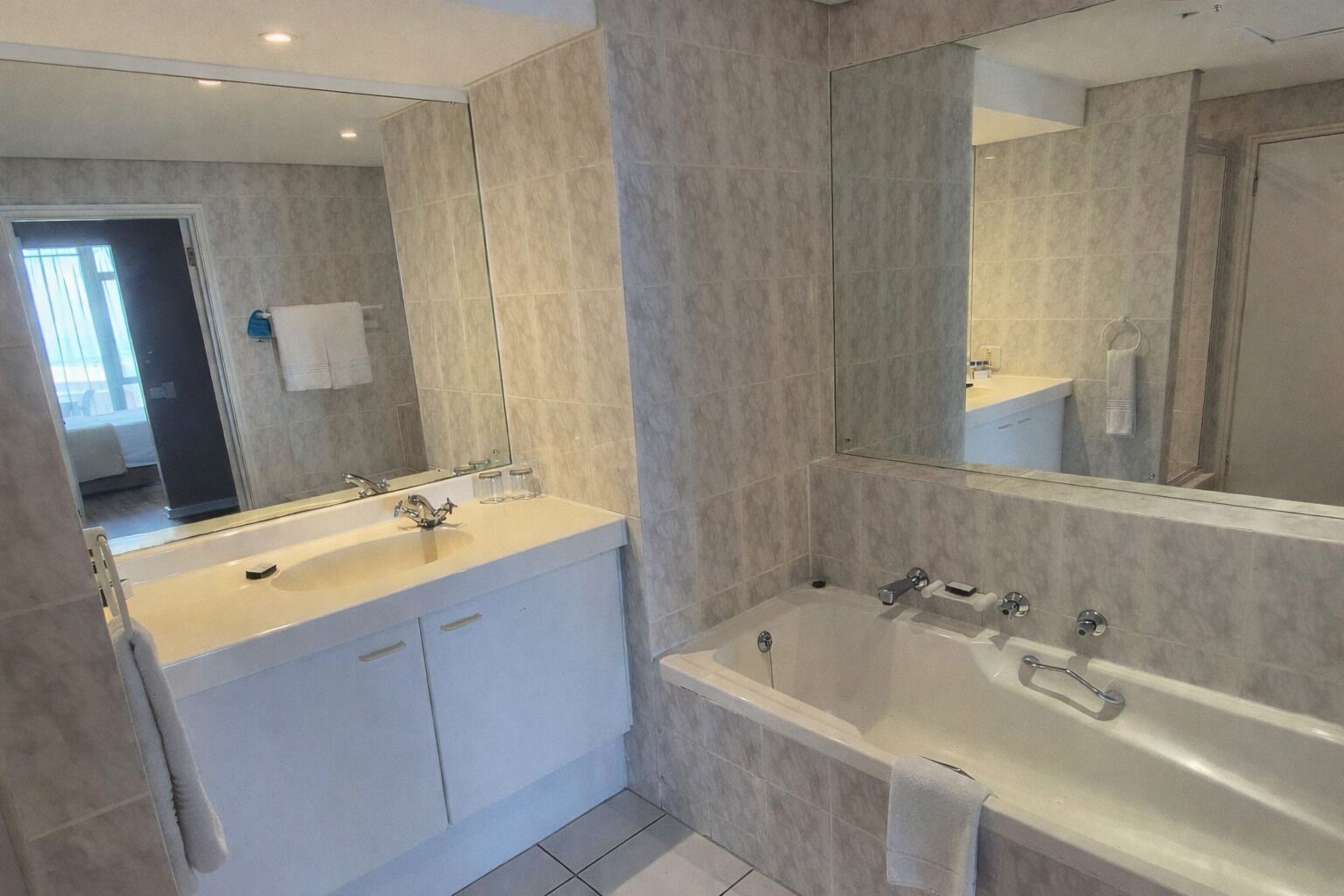 A modern bathroom with a large mirror, a bathtub, and a vanity with a sink.