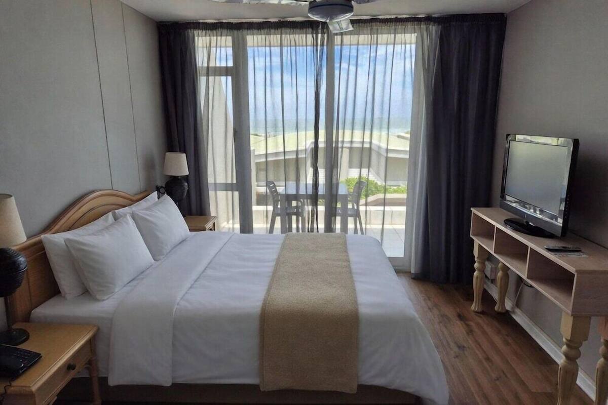 Ein Hotelzimmer mit Bett, Fernseher, Schreibtisch, Stuhl und einem Balkon mit Blick.