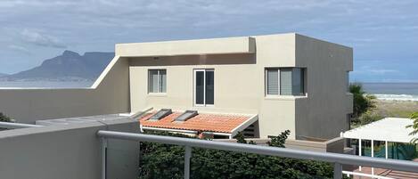 Un edificio moderno con techo plano y ventanas grandes, con vistas a una zona costera y montañas en la distancia.