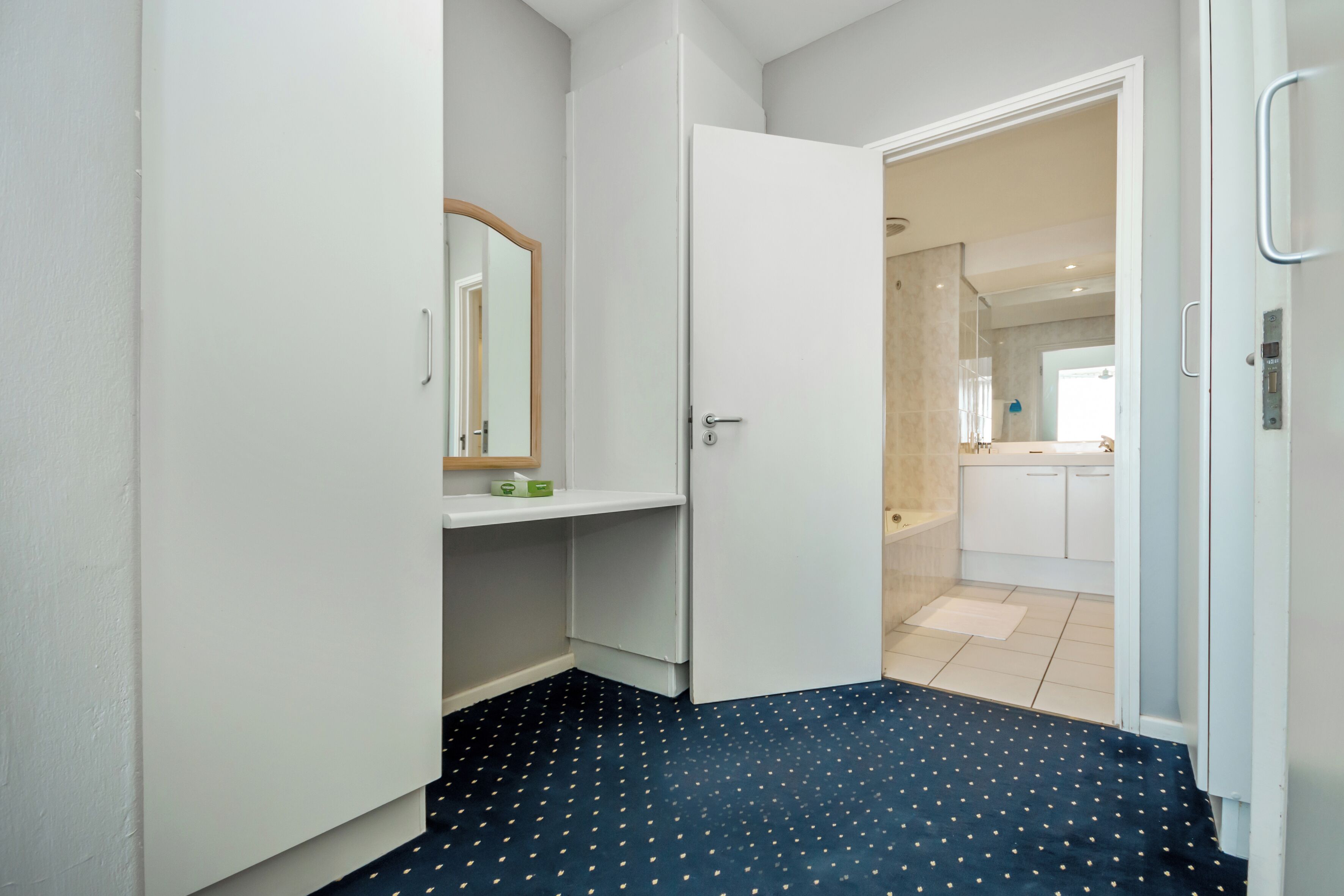 Un corridoio con una porta bianca che dà su un bagno con specchio, lavabo e water.