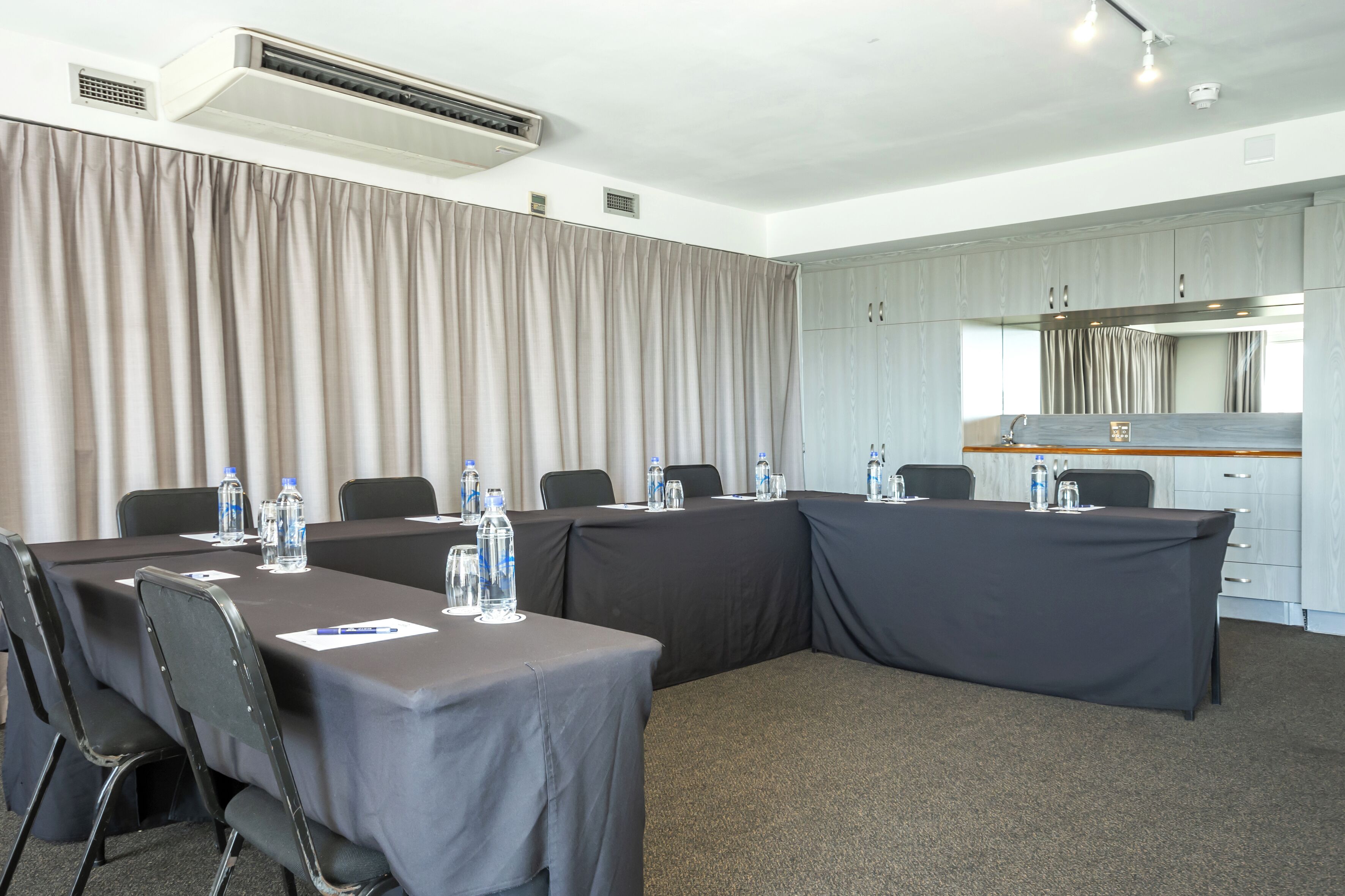 A conference room with a long table, chairs, water bottles, and a kitchenette area.